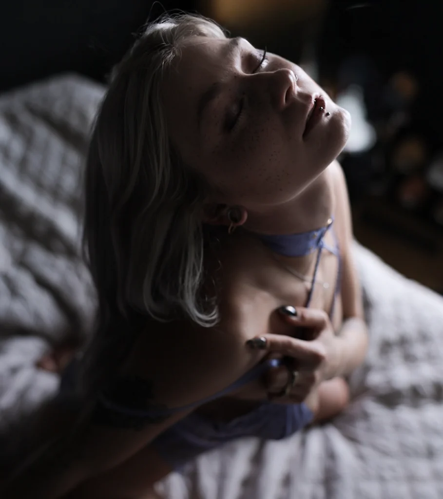 WitheredRose silberblond im hellblauen Bra-Set auf Bett – Portrait mit zurückgeworfenem Kopf, Sommersprossen und Piercings