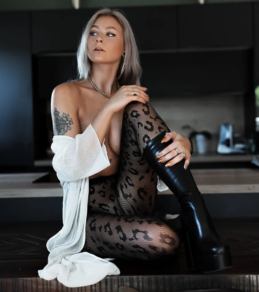 WitheredRose silberblond im weißen Cardigan und Leo-Netzstrumpfhose sitzt auf Küchenzeile – Rose-Sleeve-Tattoo
